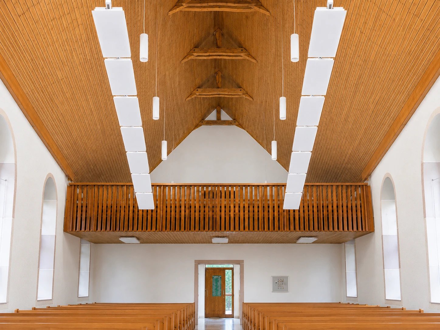 Kirchenschiff mit heller Holzdecke, darunter zwei lange Reihen weißer Infrarot-Deckenpaneele über den Bankreihen.